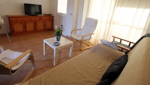 Una sala de estar con un sofá, una mesita con un florero, un mueble de madera, un televisor y una ventana con cortinas.