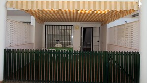 Un patio techado con valla verde, una mesa con sillas y una puerta con ventana protegida por barrotes.