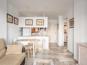 A modern kitchen with white cabinets, a dining area with a round table and chairs, and a living room with a sofa and a coffee table.
