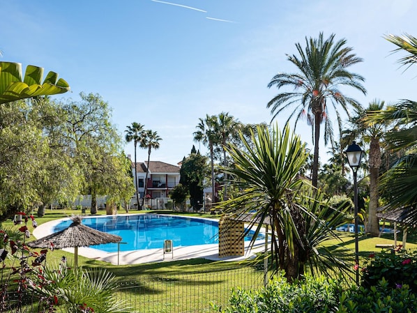 Une piscine entourée de palmiers et surmontée d’un parasol en feuilles de palmier.