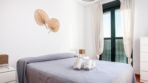 Ein Schlafzimmer mit einem Bett, einem Nachttisch, einer Lampe, einem Fenster mit Vorhängen und einem Wandventilator.