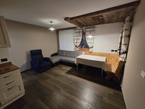 A room with a sofa, a chair, a table, wooden flooring, a ceiling with exposed beams, and a window with curtains.