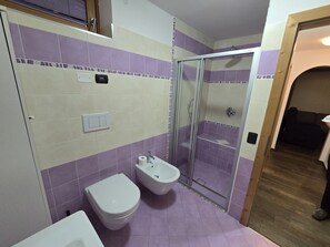 Une salle de bain équipée de toilettes, d’un bidet et d’une douche à parois de verre.