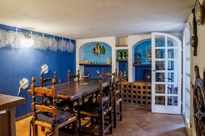 Un comedor con una mesa y sillas de madera, una pared azul con detalles decorativos y una puerta que da a otra habitación.