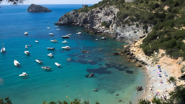 Zona costera con barcos, una playa y terreno rocoso.