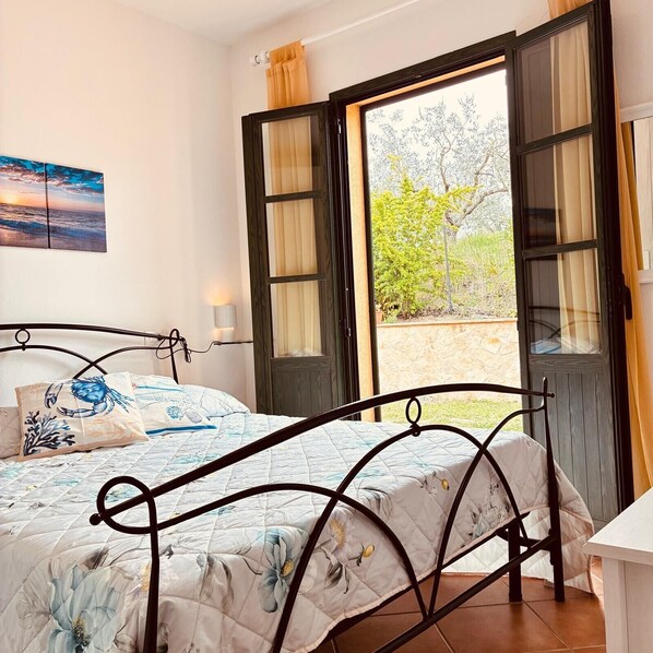 A bedroom with a bed, a nightstand, a window with curtains, and a painting on the wall. - Tuscany Retreat with Pool, Garden & BBQ near the Sea (Castellina Marittima)