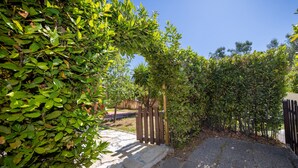 Un chemin pavé mène à une porte en bois, qui est elle-même entourée d’un feuillage verdoyant et dense.