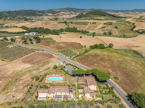 An aerial view of a residential area with a swimming pool, houses, and surrounding fields. - Tuscany Retreat with Pool, Garden & BBQ near the Sea (Castellina Marittima)