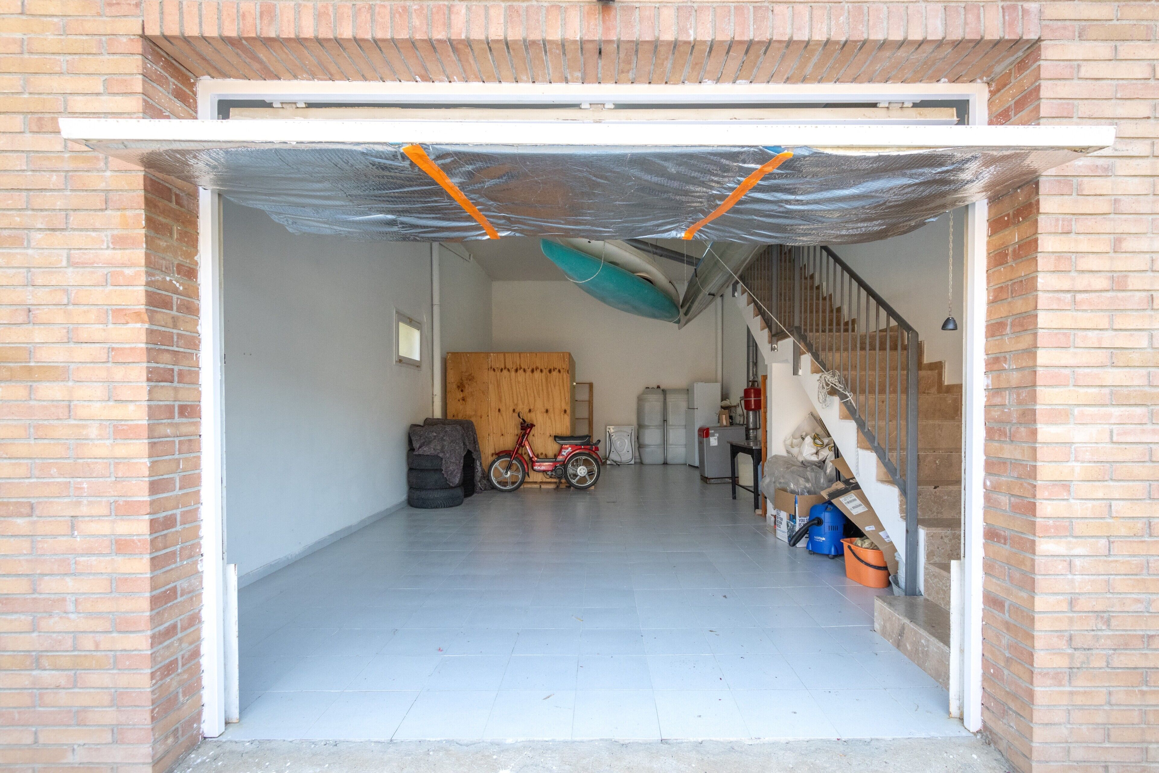 Eine Garage mit Fahrrad, Roller und überdachtem Bereich mit einer Plane.