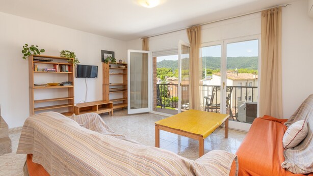 Een kamer met een bank, een tafel, een televisie en een balkon met uitzicht.