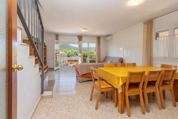 Un coin repas avec une table et des chaises, un canapé et un balcon offrant une vue sur les collines.