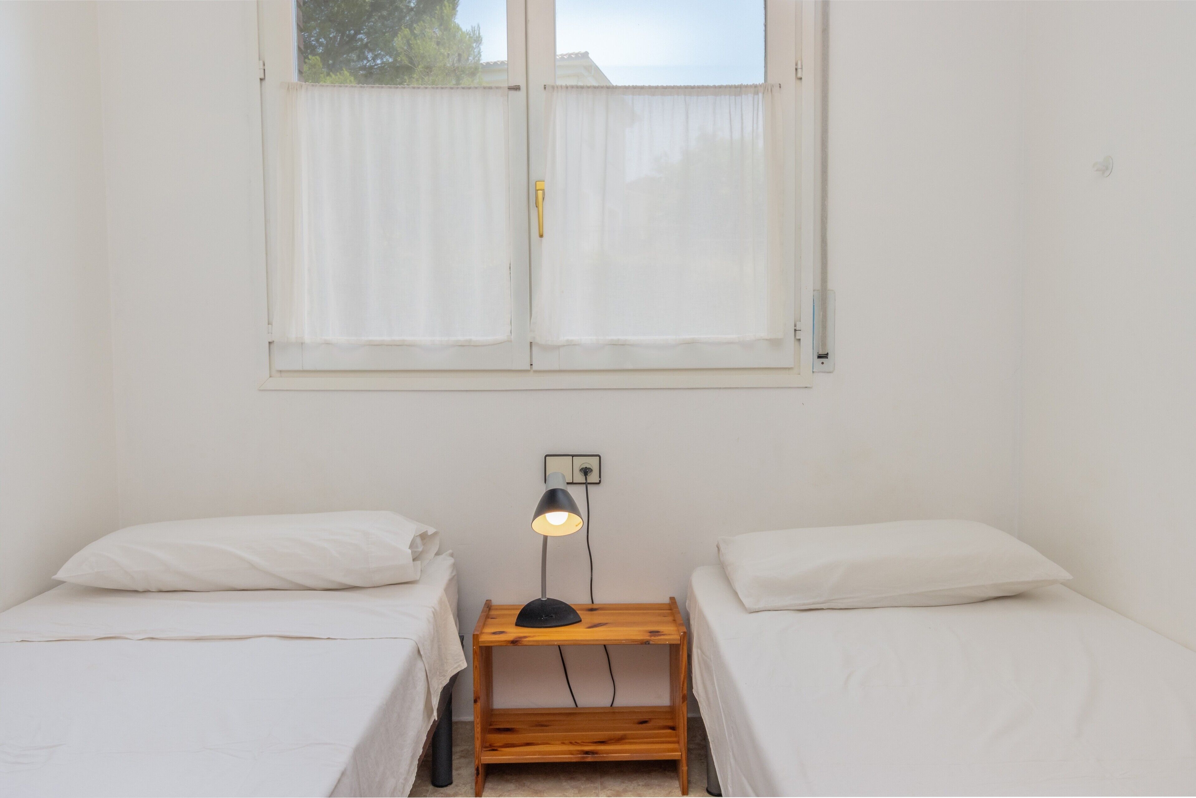 Una habitación con dos camas individuales, una mesita de noche de madera con una lámpara y una ventana con cortinas.