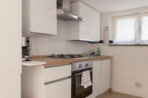 A kitchen with white cabinets, a gas stove, a sink, and a window with curtains.