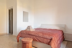 A bedroom with a bed, a small round table, a stack of towels, and a door with a patterned design.