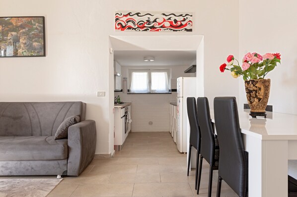 A modern living room with a grey sofa, a dining area with black chairs, a kitchen with white cabinets, and a decorative wall piece.