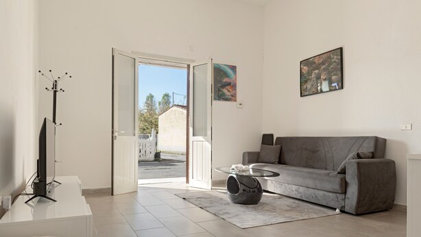 Ein modernes Wohnzimmer mit einem grauen Sofa, einem Glastisch und einem Flachbildfernseher auf einem weißen Schrank.