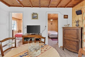 Una habitación con techo de madera, un televisor sobre una mesa de madera, una cama con manta roja y un aparador de madera.
