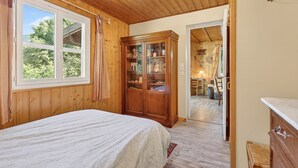 Ein Zimmer mit Holzboden, einem Bett, einer Vitrine und Blick auf einen Garten durch ein Fenster.