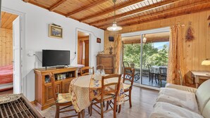 Ein Holzinterieur mit einem Esstisch, Stühlen, einer Couch, einem Fernseher und Blick durch eine Glastür.