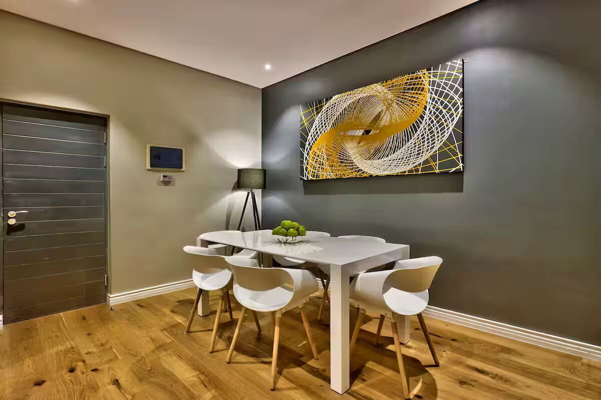 A dining area with a white table, six white chairs, and a fruit bowl.
