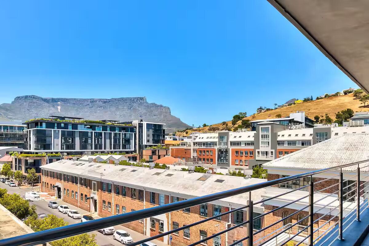 A cityscape with modern buildings, a prominent mountain in the background, and a clear blue sky.