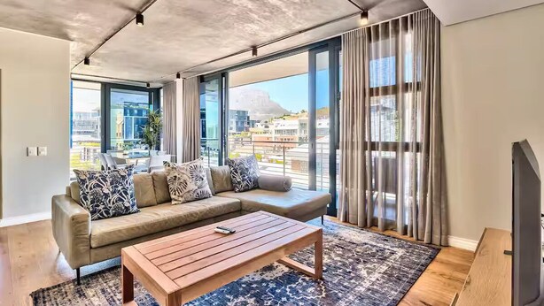 A modern living room with a sofa, a coffee table, and large windows offering a city view.