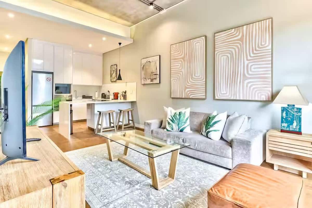 A modern living room with a glass coffee table, a grey sofa, and a wooden side table.