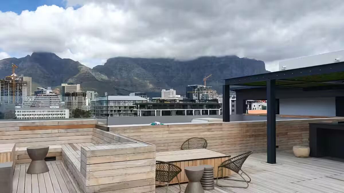 Terraço no telhado com piso de madeira, mobiliário e vista para paisagem urbana e montanhas.