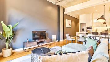 Una sala de estar moderna con un sofá, una mesa de centro y un televisor. Se observa un comedor con sillas y una mesa.