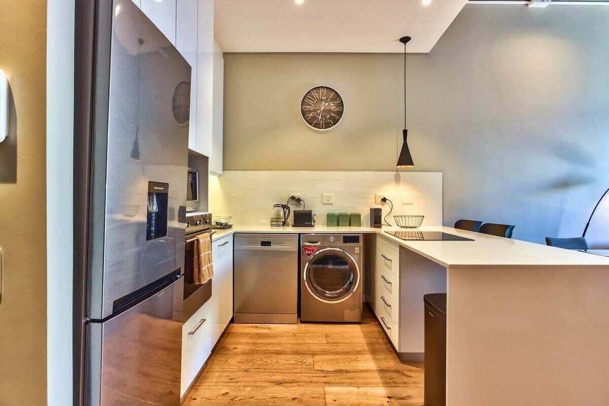 Una cocina moderna con electrodomésticos de acero inoxidable, lavavajillas, lavadora y un reloj en la pared.