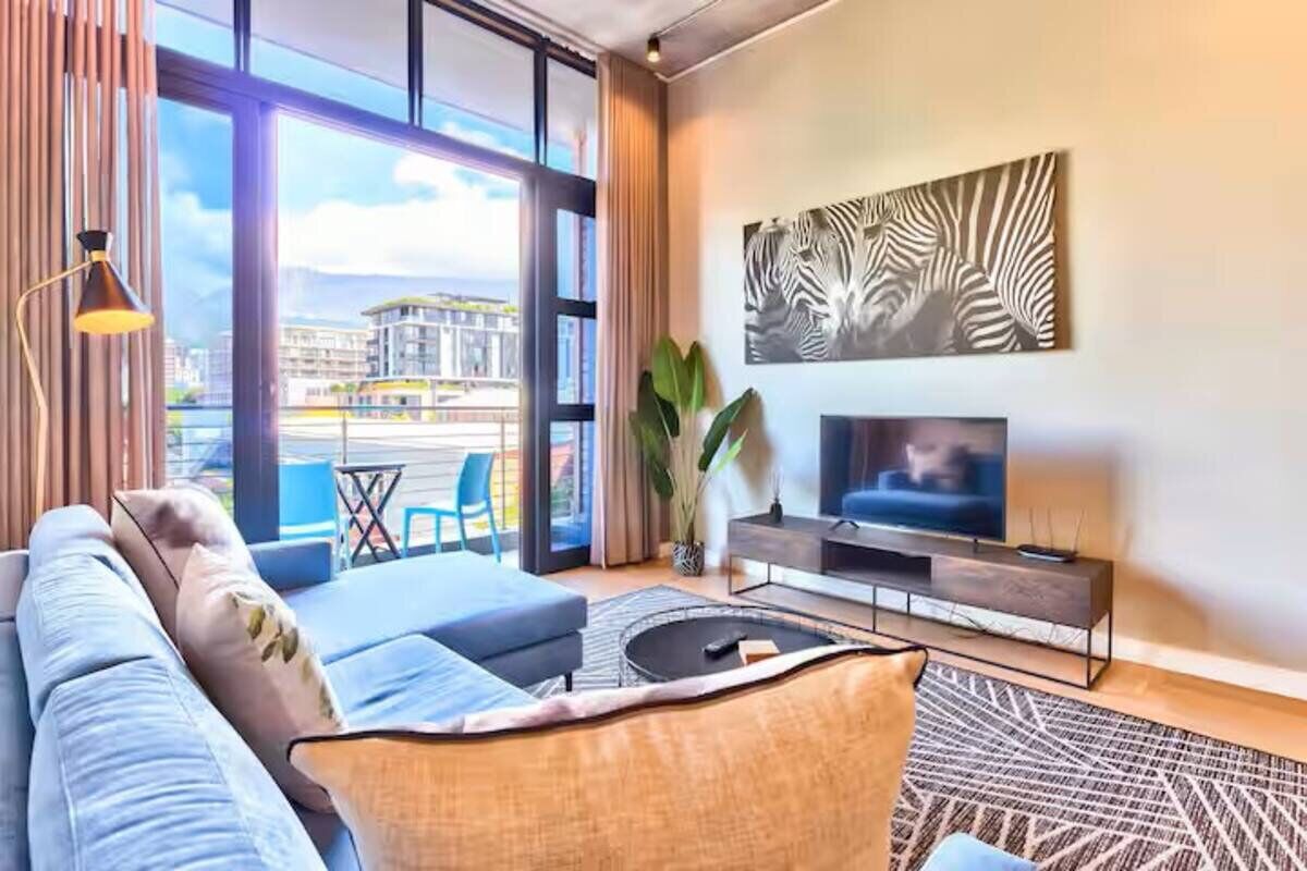 Moderni olohuone, jossa on suuri televisio, mukavat istuimet, näkymä kaupunkiin ja seeprankuvioinen taideteos.