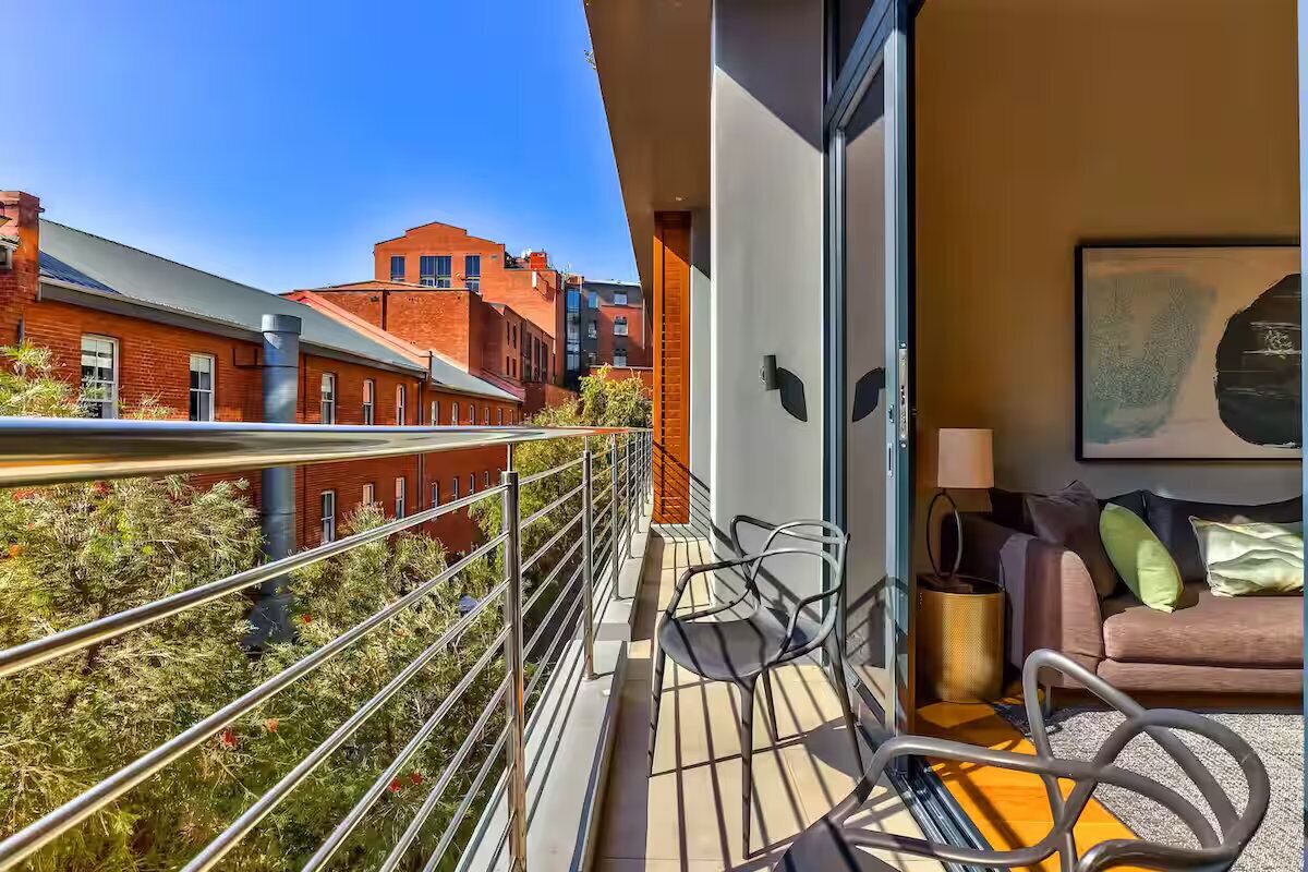 A balcony with a view of red brick buildings, a sofa, and a framed artwork.