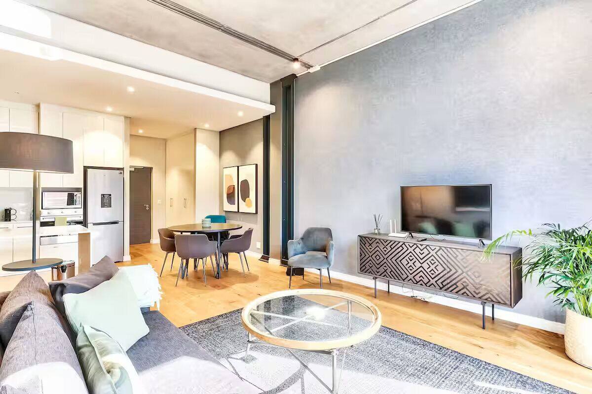 A modern living room with a sofa, a glass coffee table, a TV, and a dining area with chairs and a table.