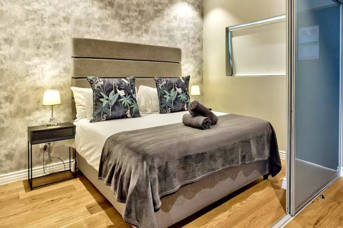 A modern bedroom with a large bed, a headboard, two bedside lamps, and a wooden floor.