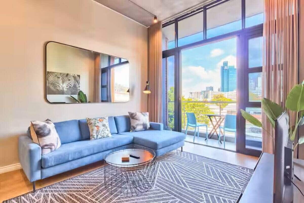 A modern living room with a blue sofa, a round coffee table, and a large window offering a city view.