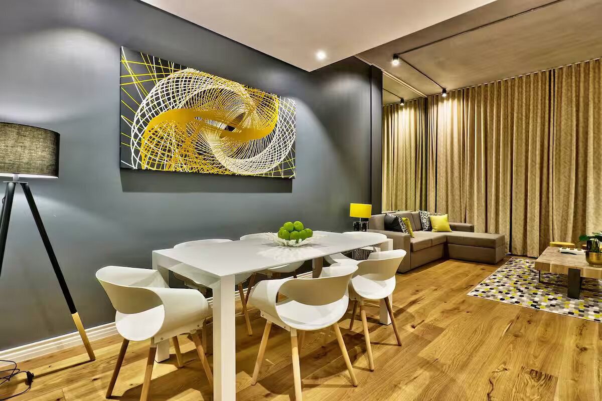 Una sala de estar moderna con una mesa de comedor blanca, sillas blancas, un sofá y un cuadro abstracto grande en la pared.