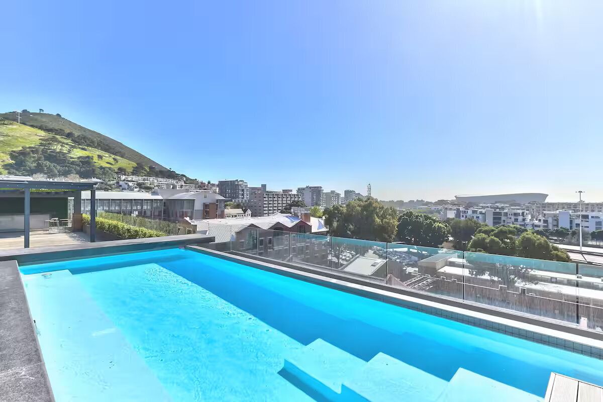 Une piscine sur le toit offrant une vue panoramique sur la ville, avec des bâtiments et une colline en arrière-plan.
