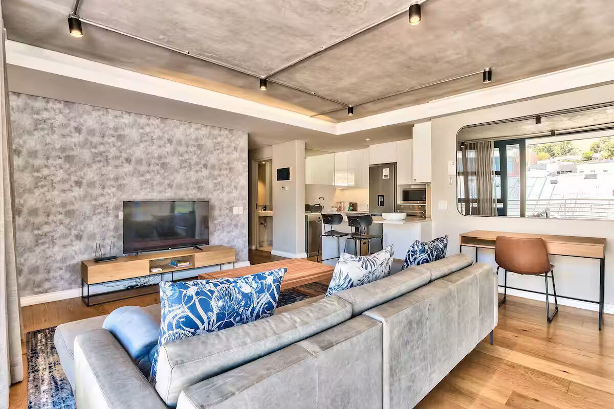 A modern living room with a large grey sofa, a flat-screen TV, and a dining area with a wooden table and chairs.