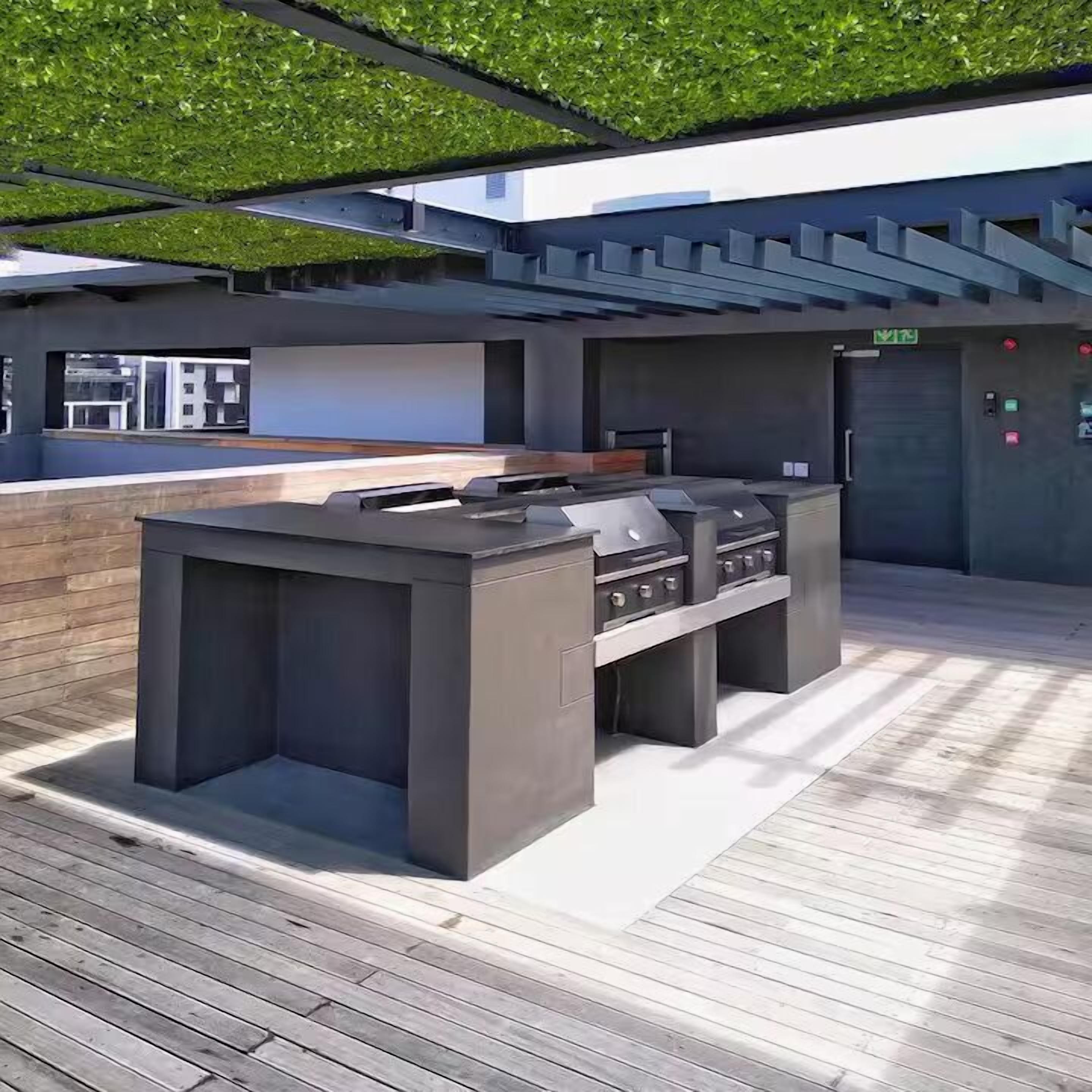 An outdoor kitchen area with a grill and bar seating, surrounded by a wooden deck and a green roof.