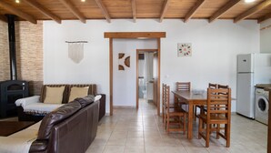 A living room with a brown leather sofa, a dining table with wooden chairs, a kitchen area with a washing machine, and a fireplace. - Holiday Home 'Alpes 2 Solo Familias' with Private Pool, Shared Terrace and Wi-Fi (Conil de la Frontera)