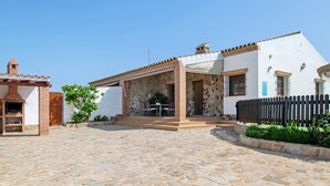 A courtyard with a stone floor, a covered patio with a table and chairs, and a brick barbecue area. - Holiday Home 'Alpes 2 Solo Familias' with Private Pool, Shared Terrace and Wi-Fi (Conil de la Frontera)