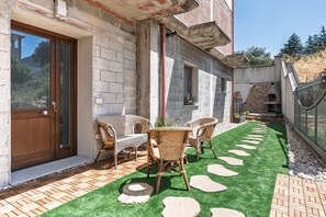 Eine Terrasse mit künstlichem Gras, Steinplatten, Korbmöbeln und einer Ziegelwand.