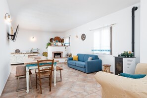 Un saló amb un sofà blau, una taula de dinar amb caires, una llar de foc i una cuina amb armaris blancs.