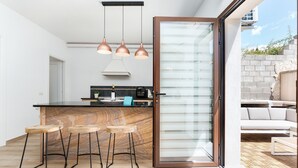 Een moderne keuken met een marmeren aanrechtblad, drie hanglampen en een schuifdeur naar een terras.
