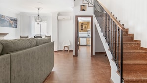 Un salon avec un canapé, un escalier doté d’une rampe et une cuisine visible à travers une porte ouverte.