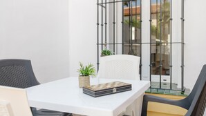 Une table blanche avec un jeu d’échecs, une petite plante et une chaise en osier.
