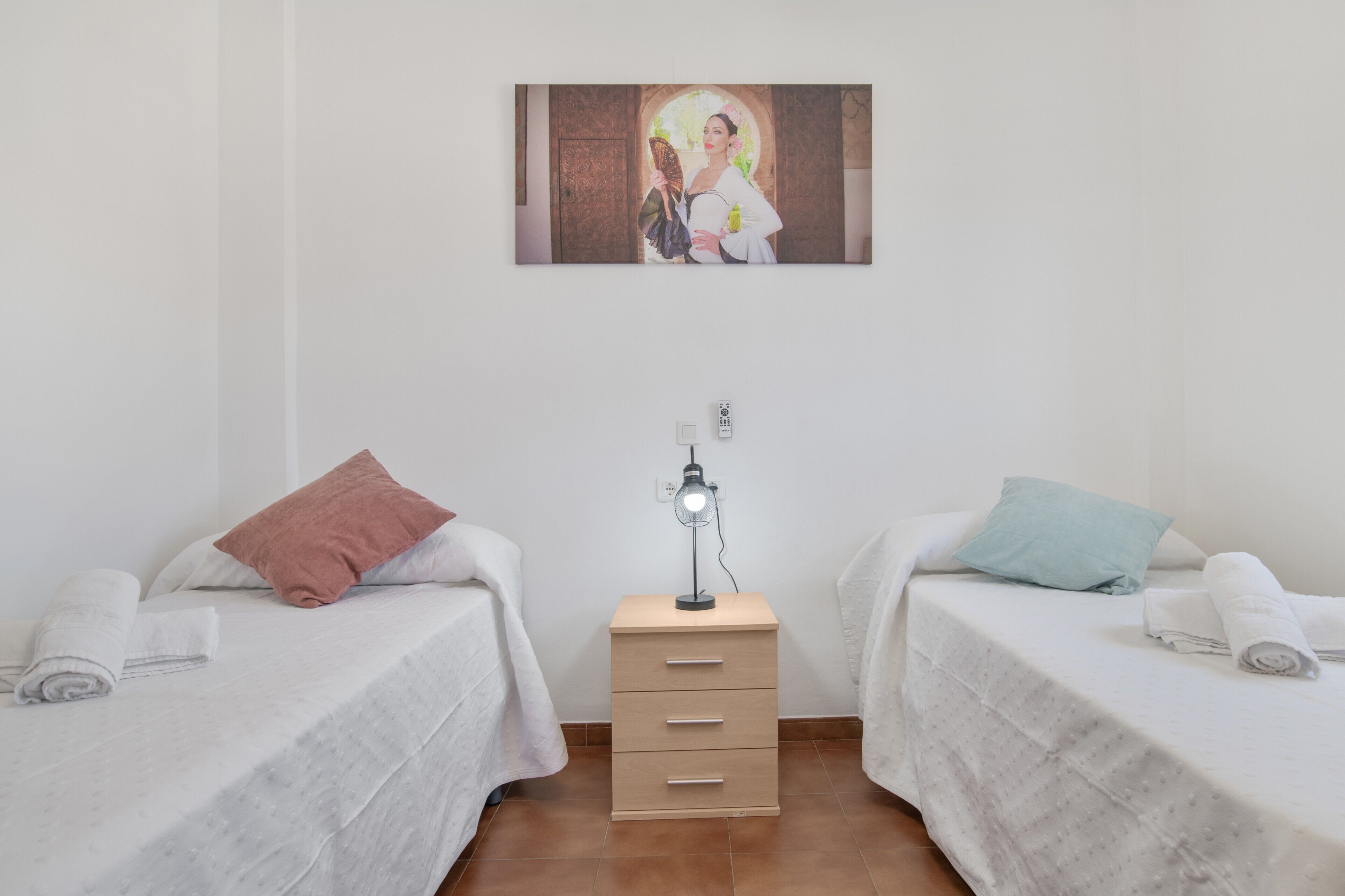Een kamer met twee bedden, een nachtkastje met een lamp en een schilderij aan de muur.