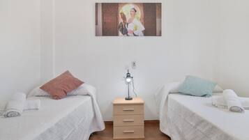 Een kamer met twee bedden, een nachtkastje met een lamp en een schilderij aan de muur.