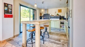 Una cocina moderna con una isla grande, taburetes de bar, iluminación colgante y vistas a través de la puerta de vidrio.