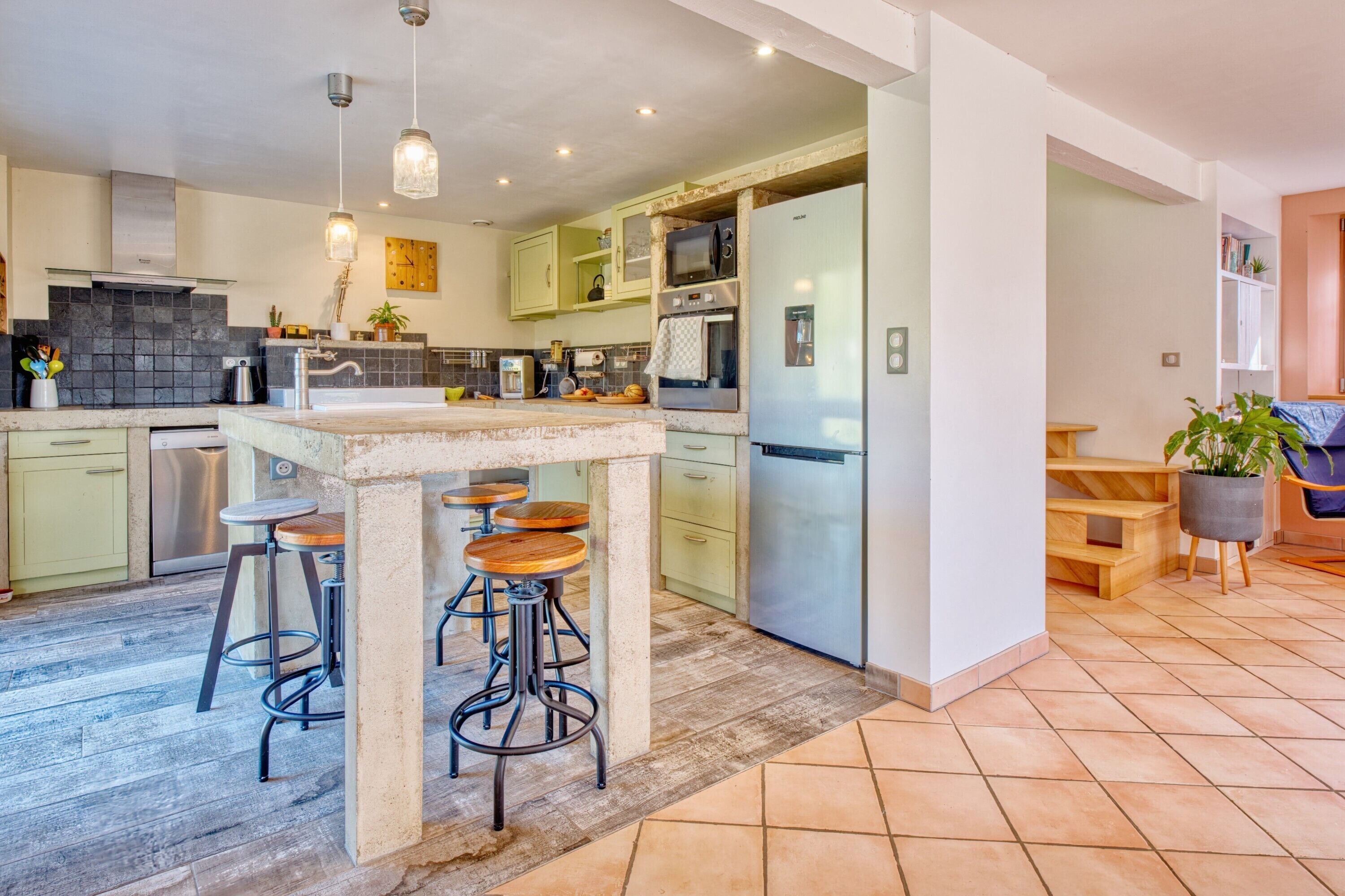 Una cocina moderna con una isla central, taburetes de bar, un refrigerador y un microondas.